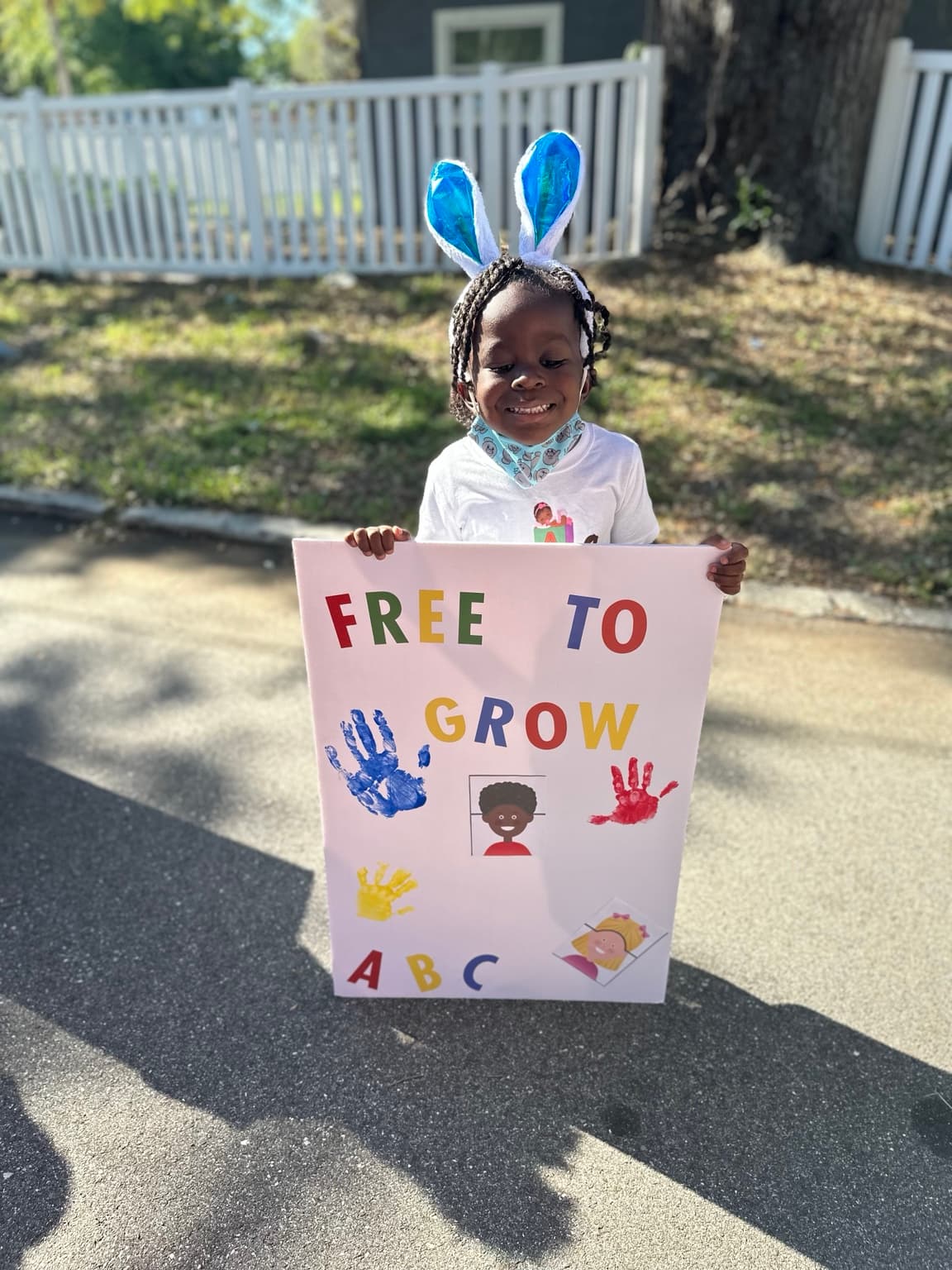 A child holding a colorful Free 2 Grow sign at a community event
